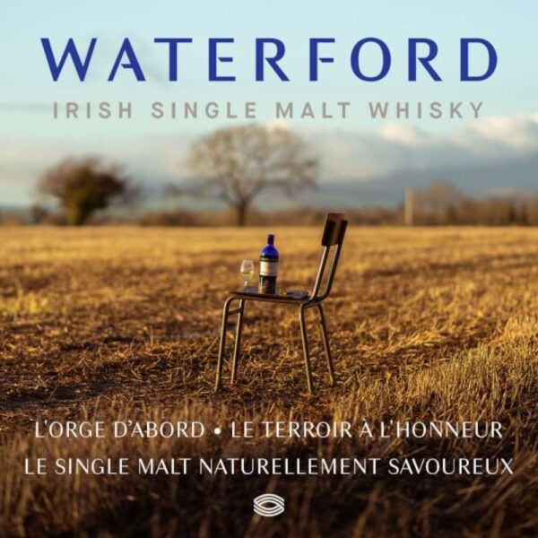 Bouteille de whisky Waterford posée sur une chaise au milieu d’un champ doré au coucher du soleil, avec un verre de dégustation, mettant en valeur l’origine naturelle et le terroir du single malt irlandais. - le club des connaisseurs